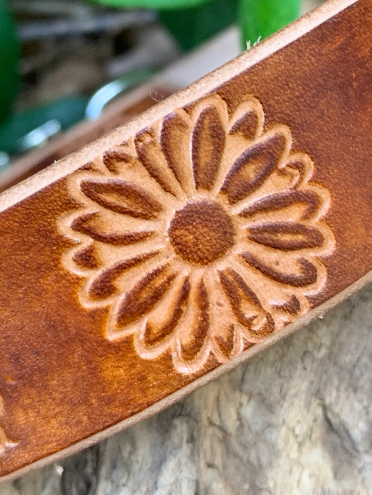 Close-up of a brown leather strap with a hand-tooled floral daisy pattern, resting on a textured wooden surface.