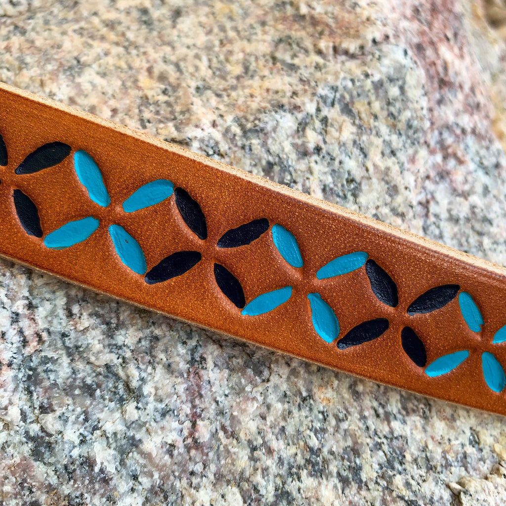 A close-up of a brown leather strap with a geometric pattern revealing turquoise blue and navy blue pattern, resting on a textured granite surface.